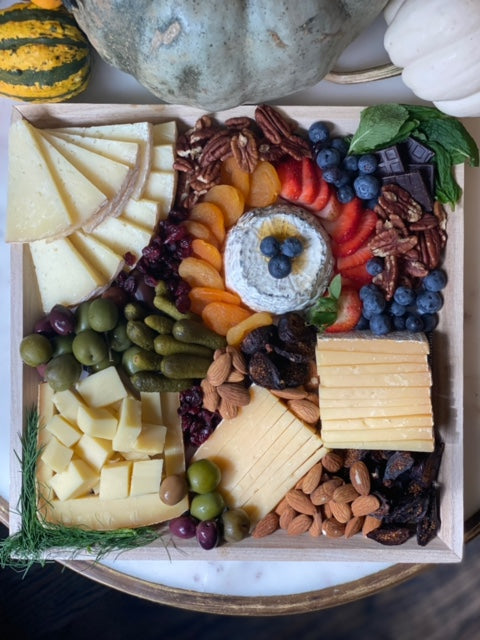 Image of an assorted cheese platter served with fresh blueberries, dried apricots, assorted olives , nuts, and pickles.