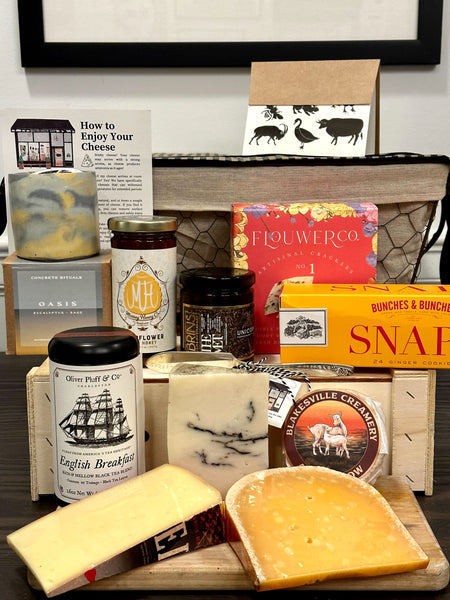 Image is of the Central Park gift basket contents. Includes: candle, honey, jam, crackers, cookies, tea, assorted cheeses, and a card. 