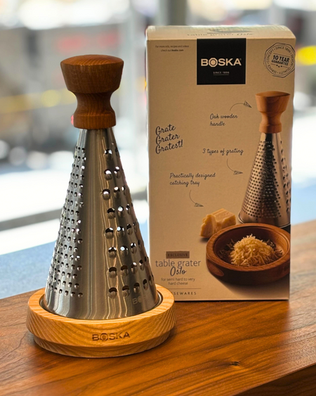 Image is of the large BOSKA cheese grater in front of its box on a wooden table.